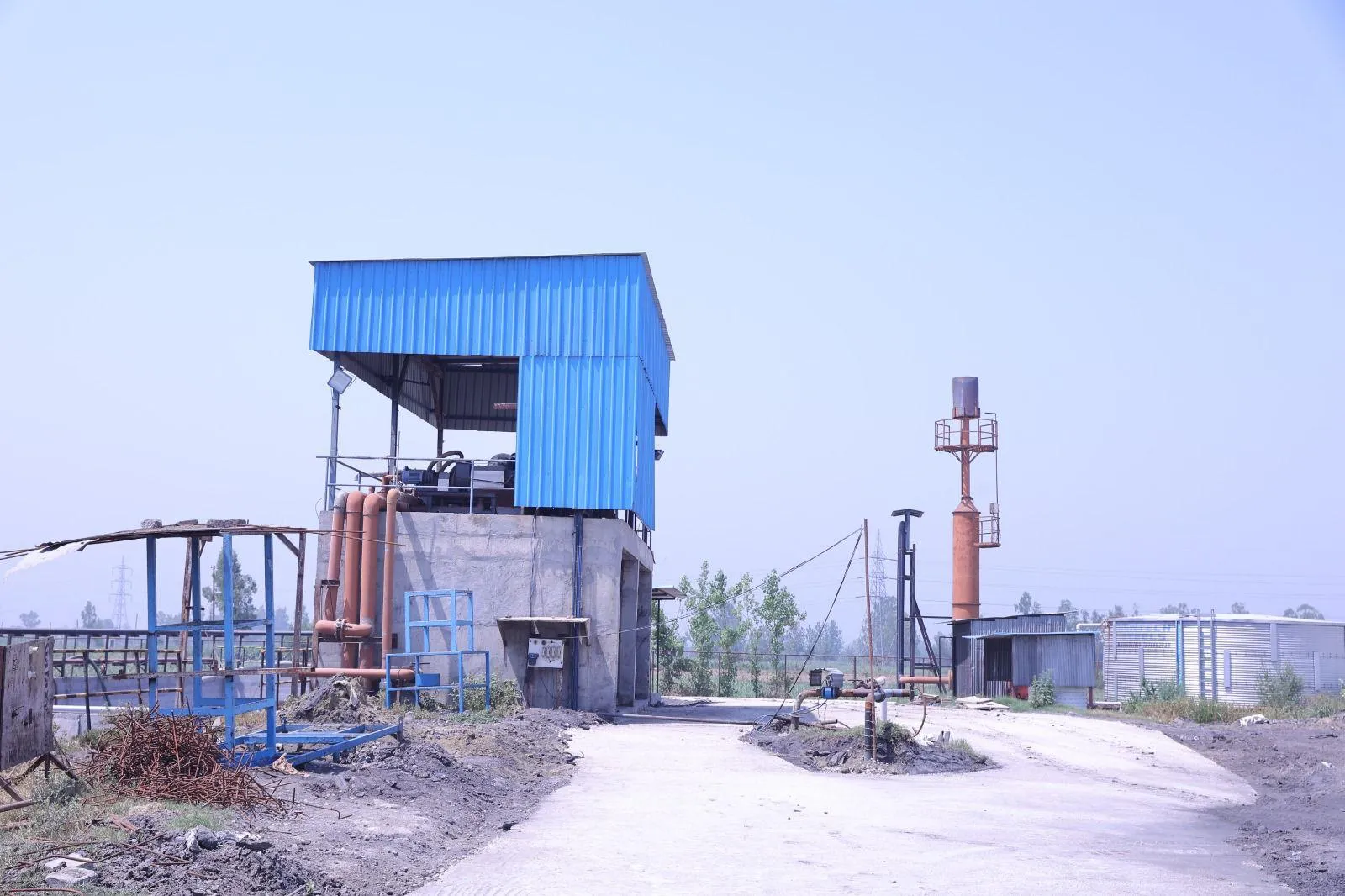 The dewatering building and flare at the Circle CBG Meerut plant, with the access road and open fields beyond